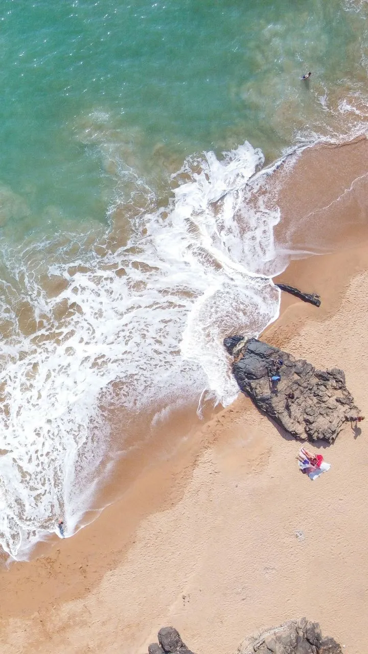 Turquoise waves washing over golden sand on a Gokarna beach, seen from above