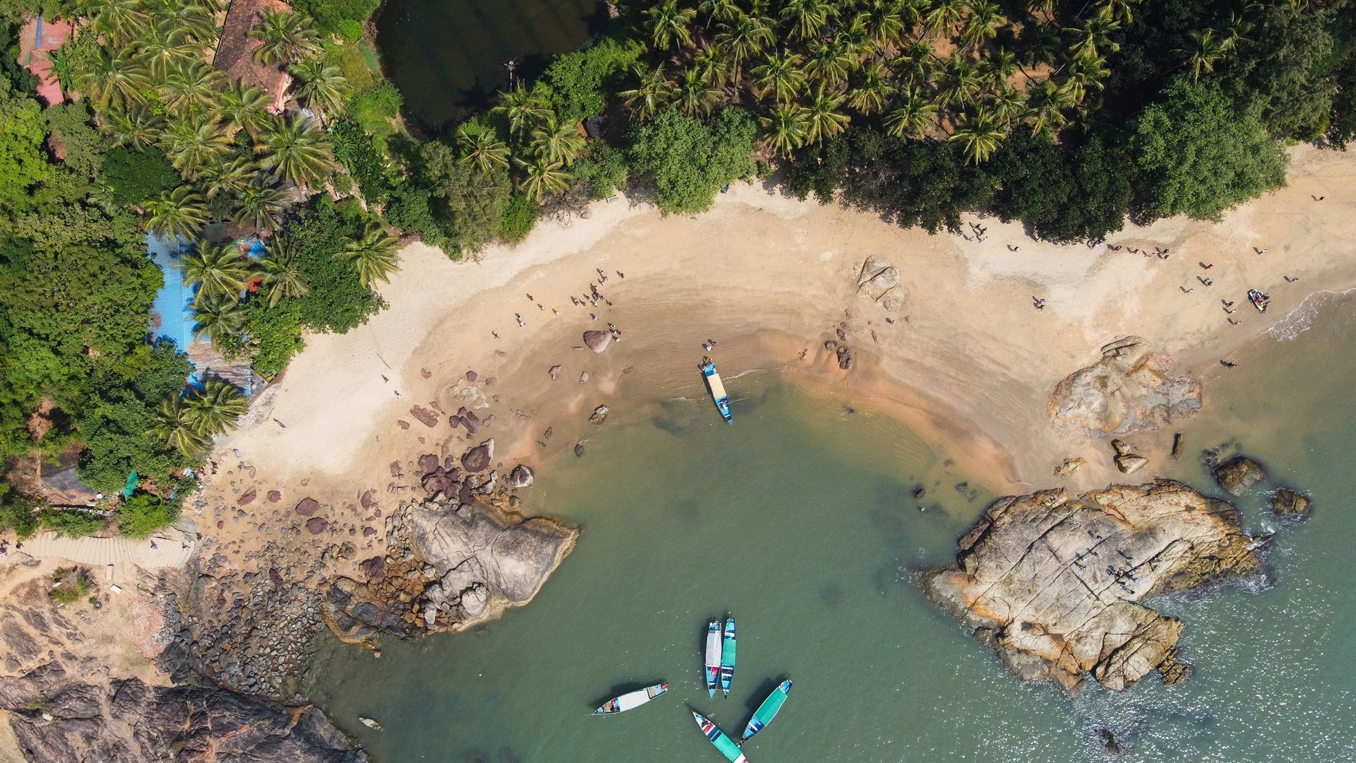 Aerial view of a Gokarna beach with turquoise water, boats on golden sand and palm-lined headlands