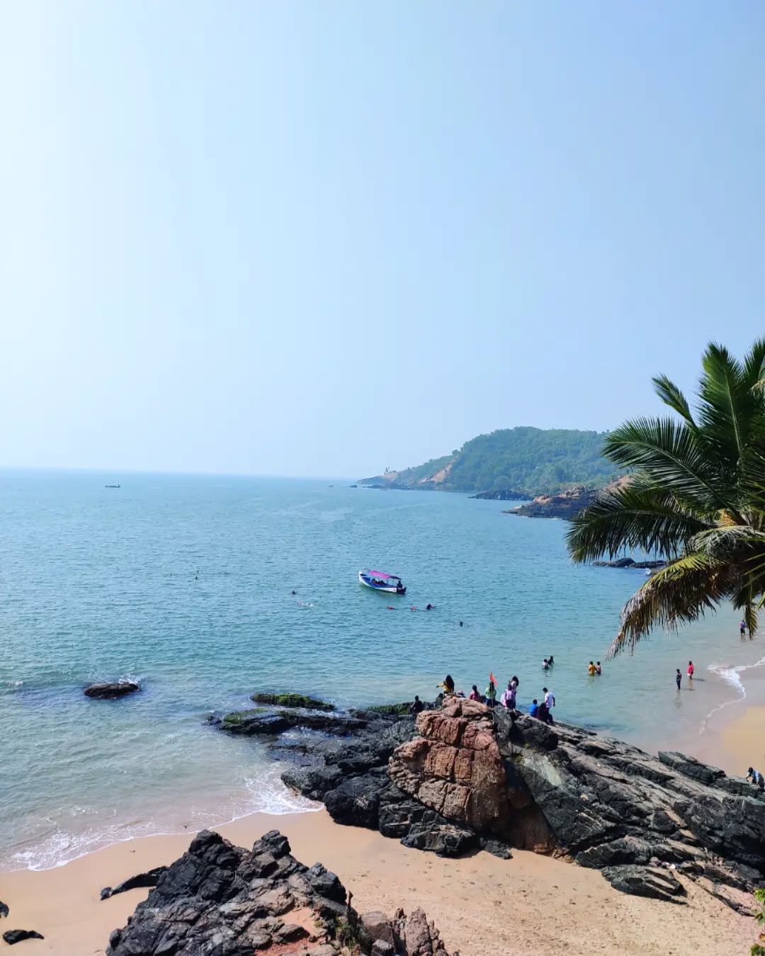Clifftop view over the turquoise bay at Om Beach in Gokarna, with a small boat and palm fronds
